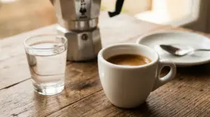 Tazzina di caffè espresso con bicchiere d'acqua su tavolo di legno